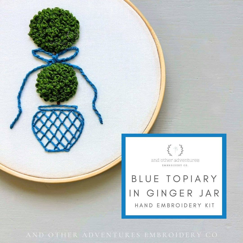 Embroidery hoop with blue topiary design and text about embroidery kit on a light gray background