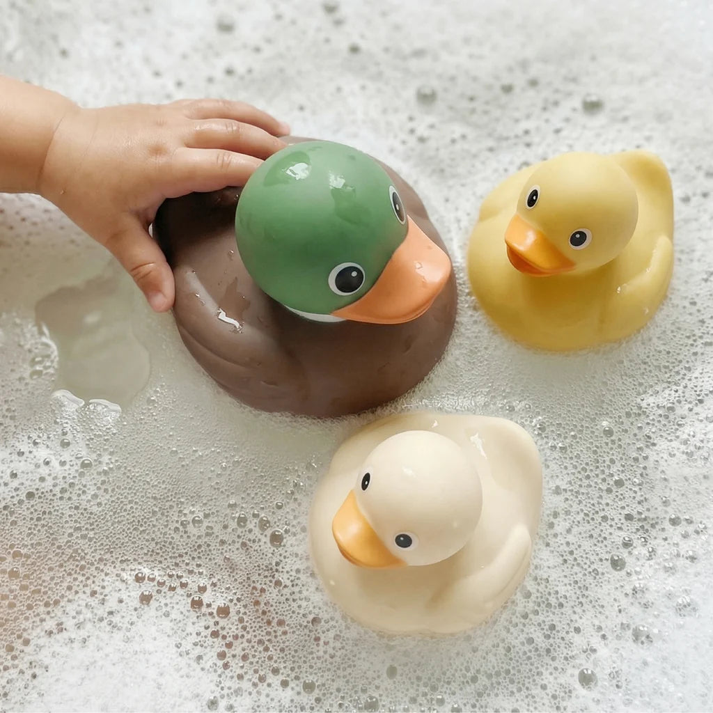 3 rubber duck bath toys in bubble bath with baby's hand