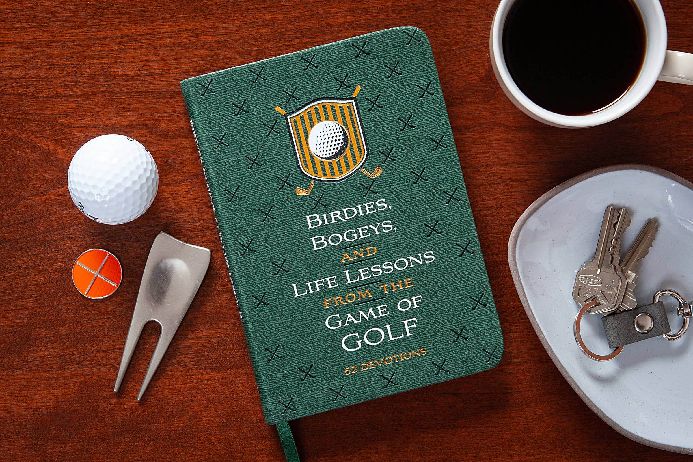 Green notebook titled 'Birdies, Bogeys, and Life Lessons from the Game of Golf' on a wooden surface with a golf ball, divot tool, and coffee.