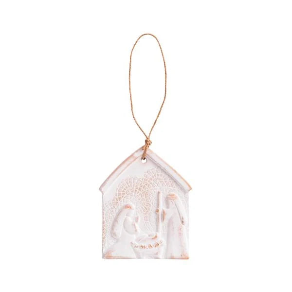 A small house-shaped hanging ornament with a rope loop at the top, featuring a white embossed nativity scene with soft blush-pink and warm beige tones, shown on a plain white background.