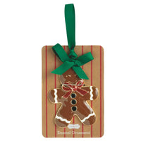 A gingerbread man enamel ornament on a brown kraft paper card with red stripes, featuring a green ribbon loop at the top.