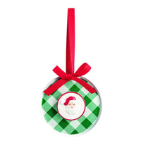 A round Christmas ornament with a green and white gingham pattern, featuring a red ribbon loop at the top and a central circular cutout showing a smiling Santa face.