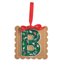 A decorative hanging ornament shaped like the letter B, made from brown kraft cardstock with a green glitter center printed with holiday light patterns, tied with a red ribbon, on a plain white background.