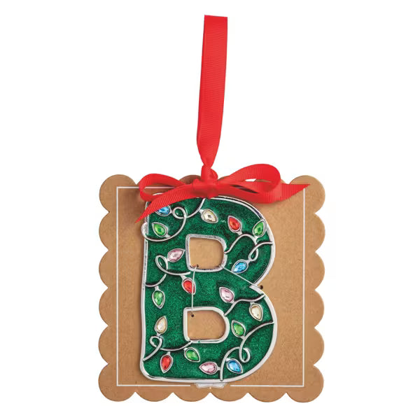 A decorative hanging ornament shaped like the letter B, made from brown kraft cardstock with a green glitter center printed with holiday light patterns, tied with a red ribbon, on a plain white background.