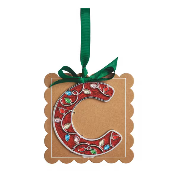A decorative hanging ornament shaped like the letter C, featuring a red background with jeweled embellishments in green, blue, and white, mounted on a brown kraft paper tag with a green ribbon loop.