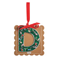 A decorative hanging ornament shaped like the letter D, with a green glitter wreath design outlined in silver and decorated with colorful rhinestones, attached to a brown scalloped card with a red ribbon loop.