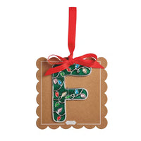 A decorative hanging ornament shaped like the letter F, mounted on a brown kraft paper tag with scalloped edges. The letter is decorated with a green holiday light pattern, and the tag is tied with a red ribbon and hanging loop against a plain white background.