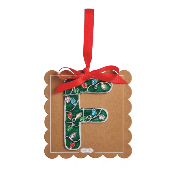 A decorative hanging ornament shaped like the letter F, mounted on a brown kraft paper tag with scalloped edges. The letter is decorated with a green holiday light pattern, and the tag is tied with a red ribbon and hanging loop against a plain white background.