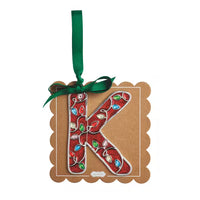 A decorative hanging ornament shaped like the letter K, made from red ribbon wrapped with colorful jewel embellishments, attached to a brown kraft paper tag with a green ribbon loop, on a plain white background.