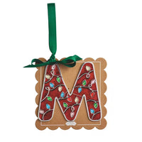 A decorative hanging ornament shaped like the letter M, made from brown kraft cardstock with a red glitter center, white wire outlines, and colorful jewel embellishments. A green ribbon loop is attached at the top.