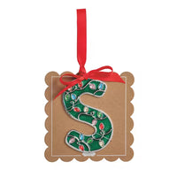 A decorative hanging ornament shaped like a kraft paper tag with scalloped edges, featuring a large embroidered letter S on a green background with multicolored Christmas light details and a red ribbon loop at the top.