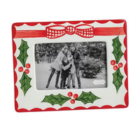 A rectangular ceramic picture frame with a festive Christmas design, featuring a red and white scalloped border, a red bow at the top, green holly leaves, and red berries. The center is blanked out with a placeholder family photo.