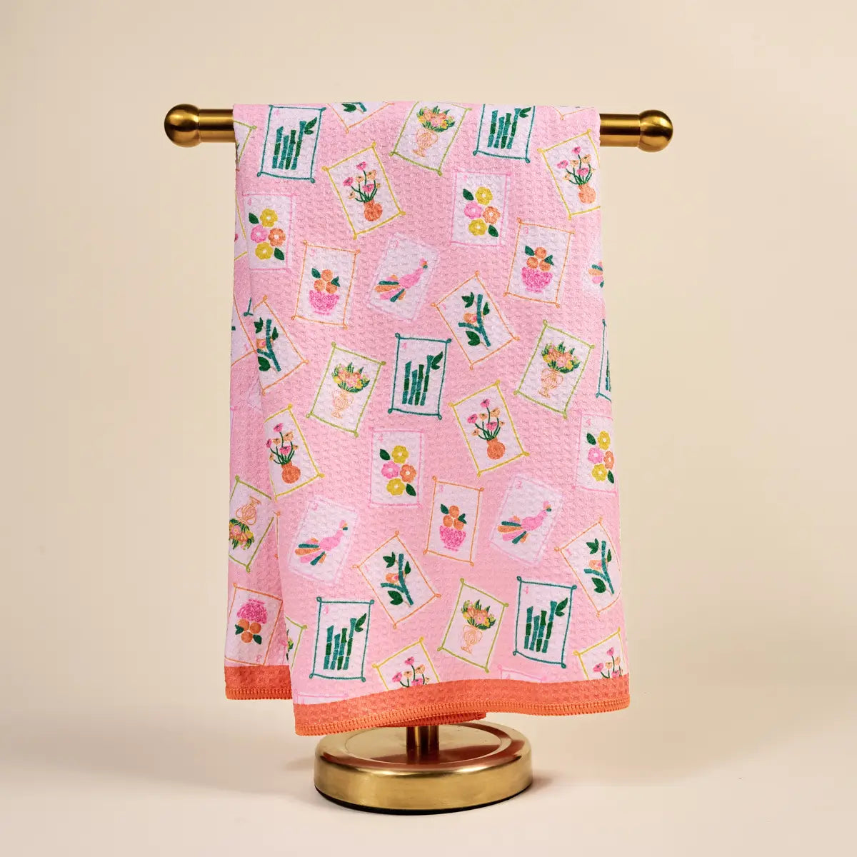 Pink towel with floral patterns hanging on a gold towel rack against a beige background