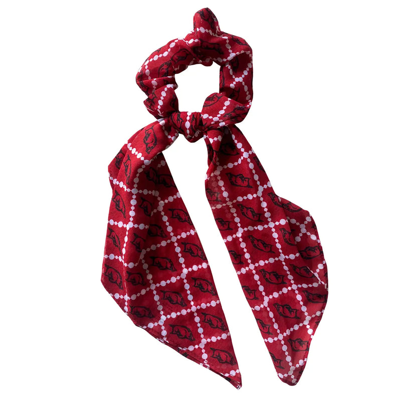 A red fabric hair scrunchie with a tied bow, featuring a white dotted diamond lattice pattern with black elephant silhouettes, set against a plain white background.