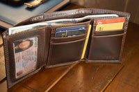 Brown leather wallet open on a wooden surface with various cards and an ID card visible.