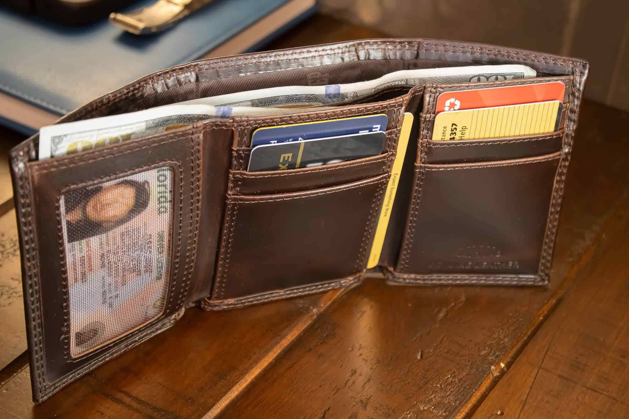 Brown leather wallet open on a wooden surface with various cards and an ID card visible.