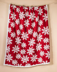 A red curtain panel with a white snowflake pattern and a white faux-fur trim, hanging against a plain beige wall.