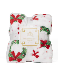 Folded Christmas-themed throw blanket with red bows and green leaves on a white background