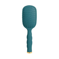 A teal green paddle hairbrush with a textured silicone bristle head and a wavy, ribbed handle, finished with a small gold accent ring at the base, shown on a solid white background.