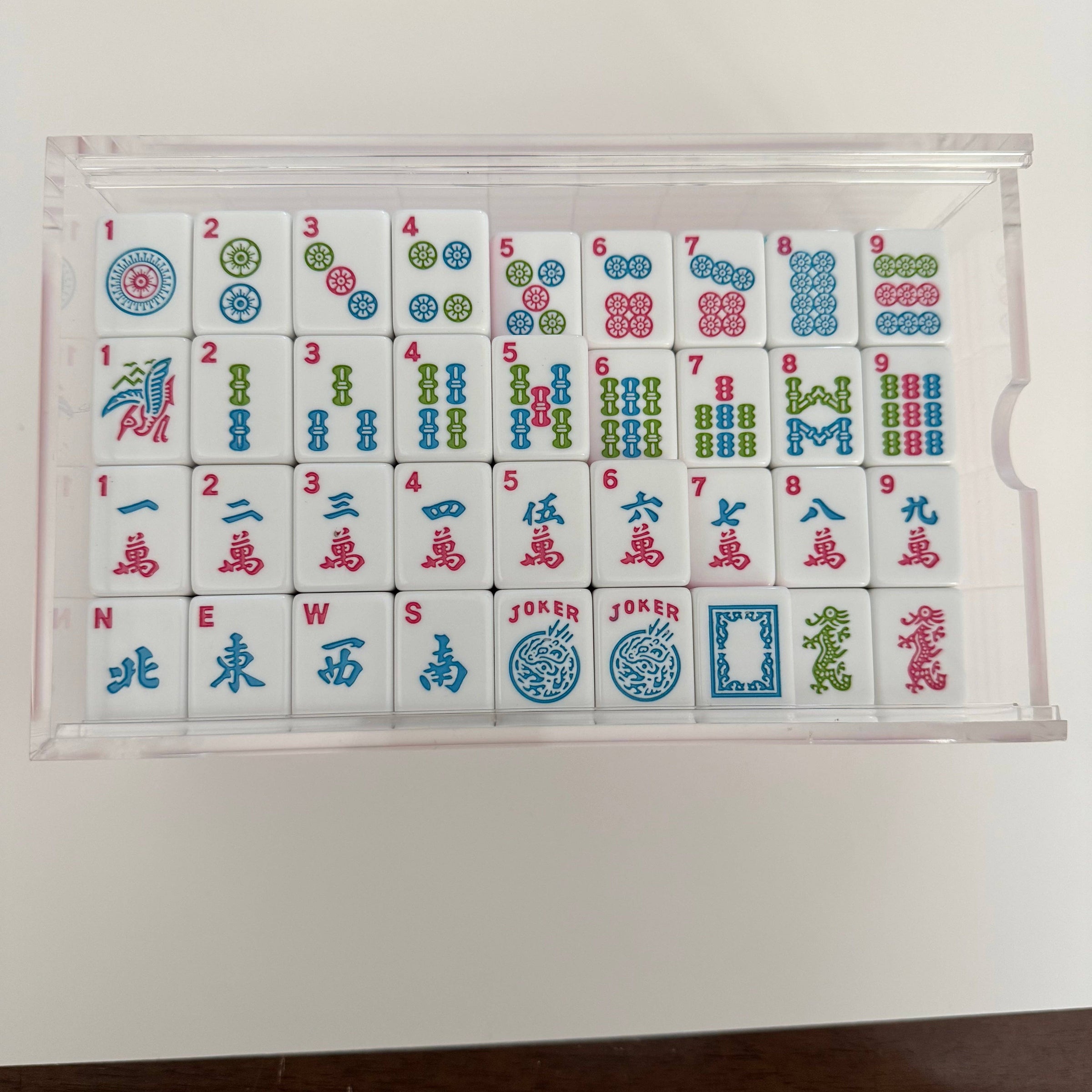 Set of Mahjong tiles in a clear plastic case on a white background
