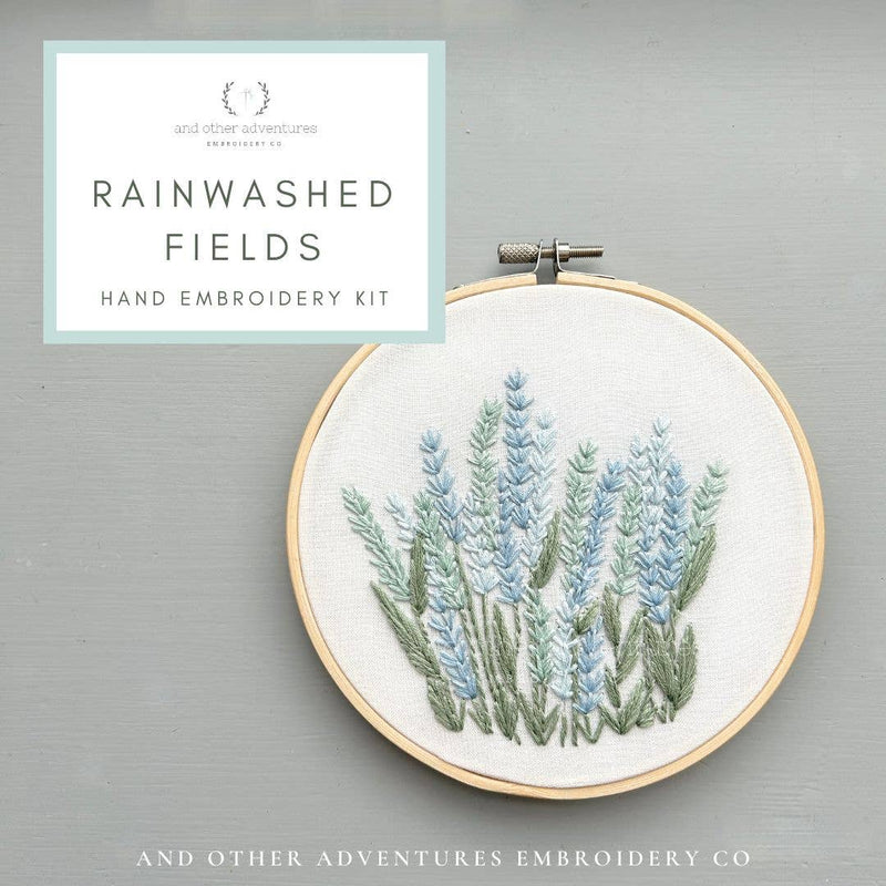 Hand embroidery kit with floral design in a hoop on a gray background, featuring the brand 'And Other Adventures Embroidery Co'.