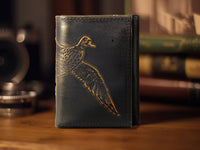 Black leather wallet with bird embossing on a wooden surface with books in the background