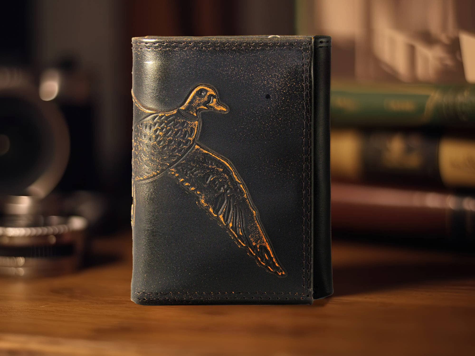 Black leather wallet with bird embossing on a wooden surface with books in the background