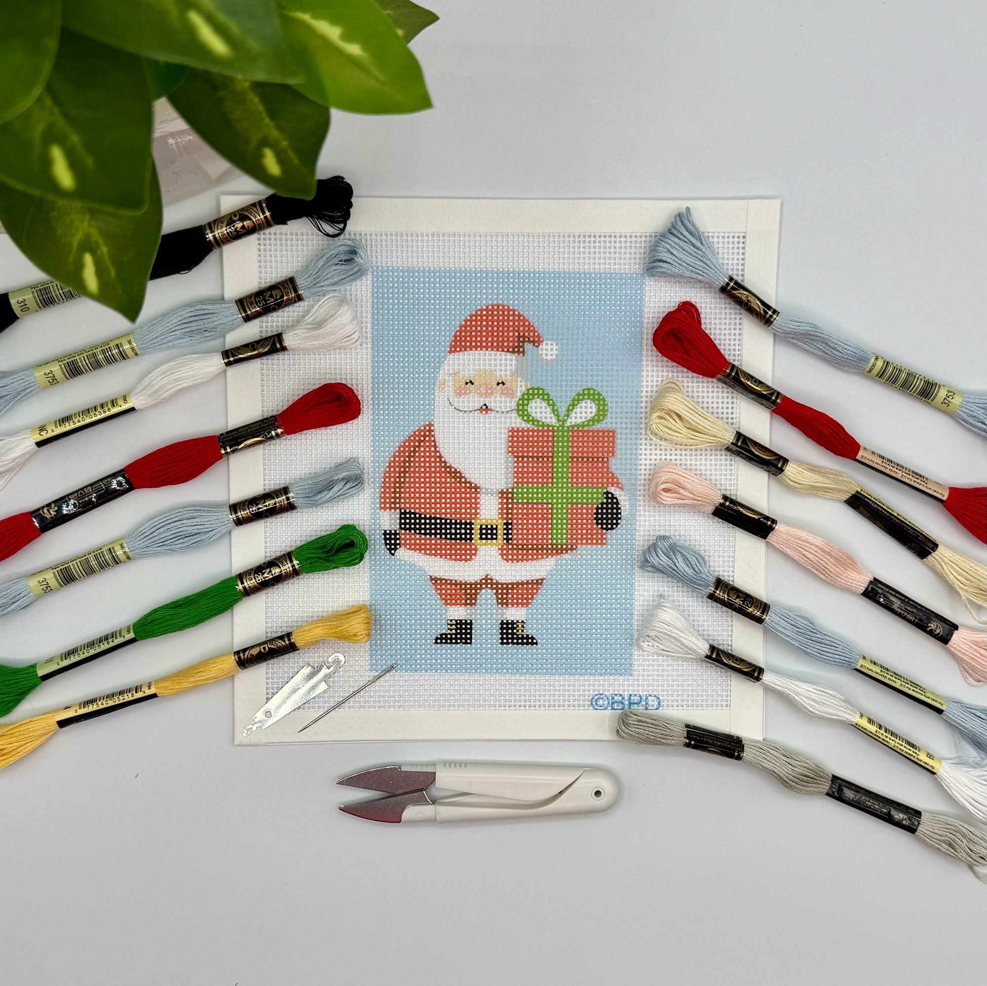 Cross-stitch kit with Santa Claus design and embroidery threads on a light gray background