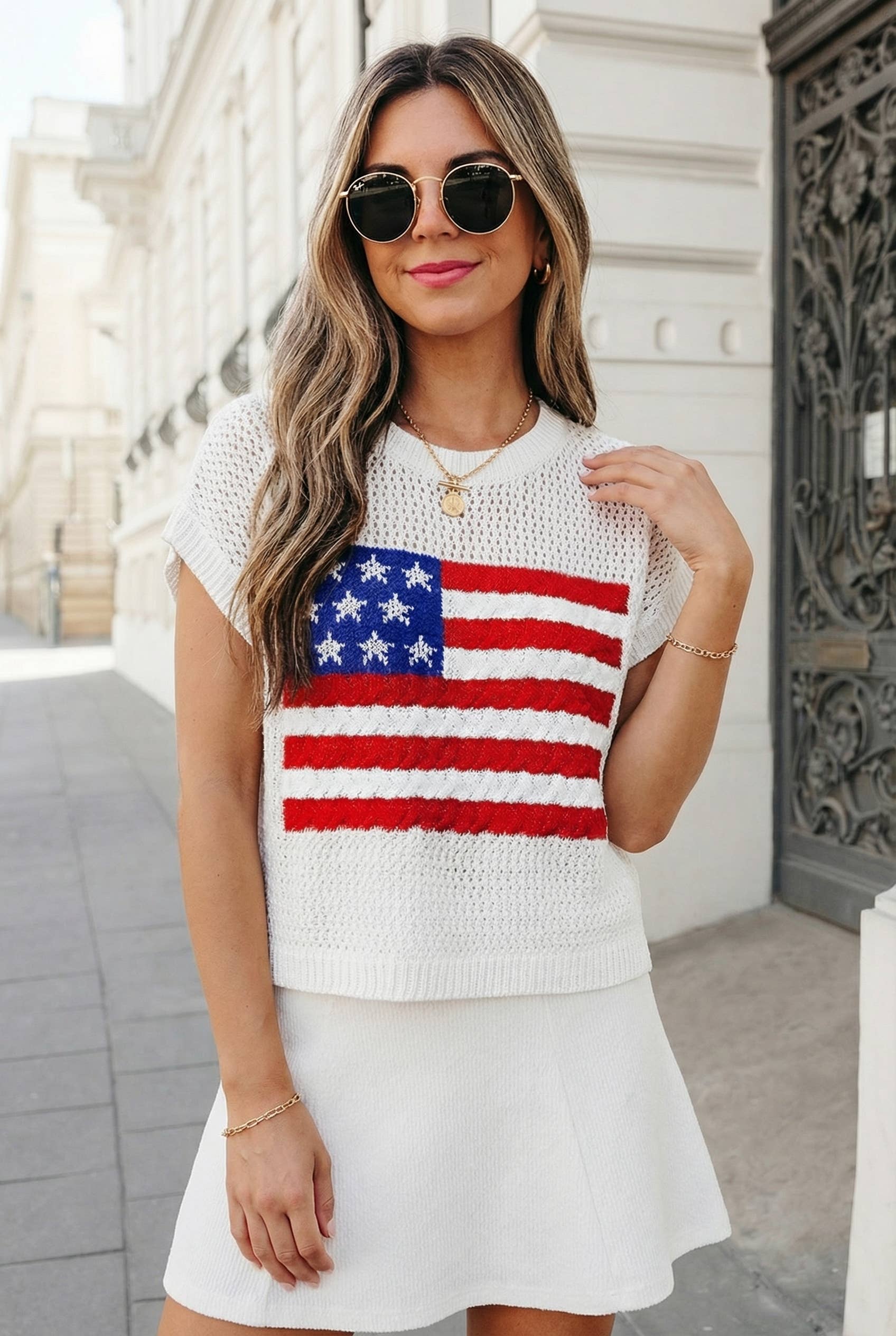 Woman wearing a white sweater with an American flag design outdoors.
