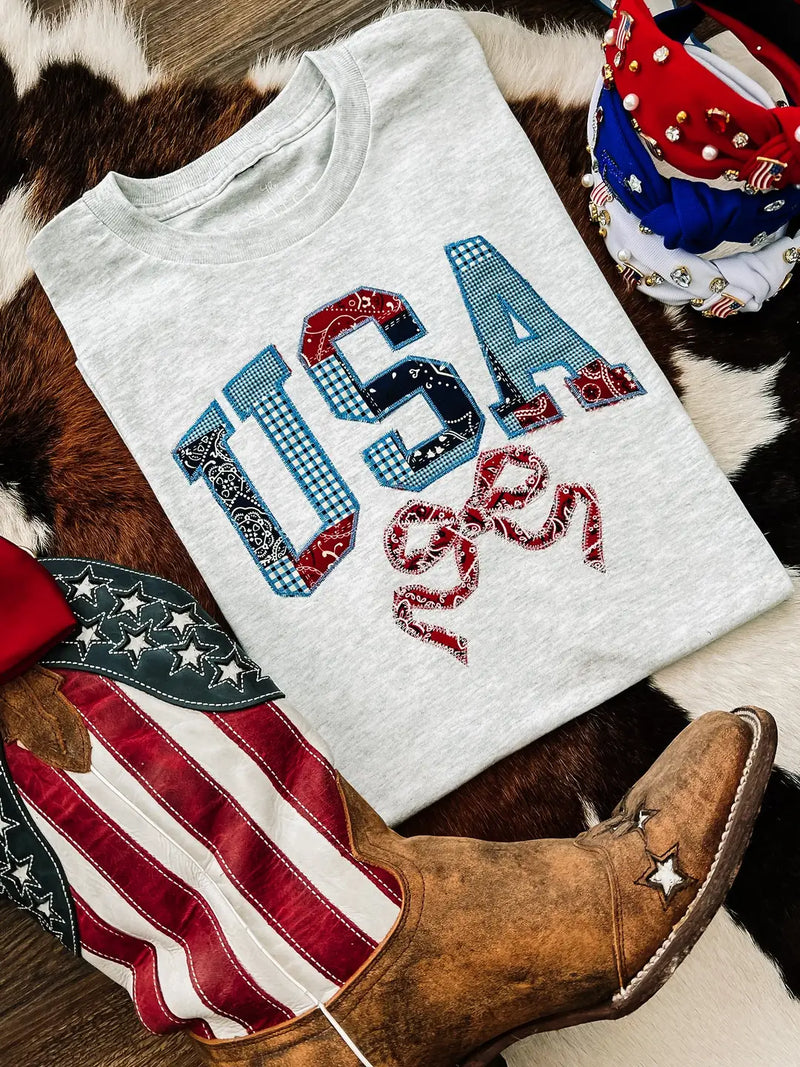 White t-shirt with 'USA' design on a cowhide rug with boots and decorative items.