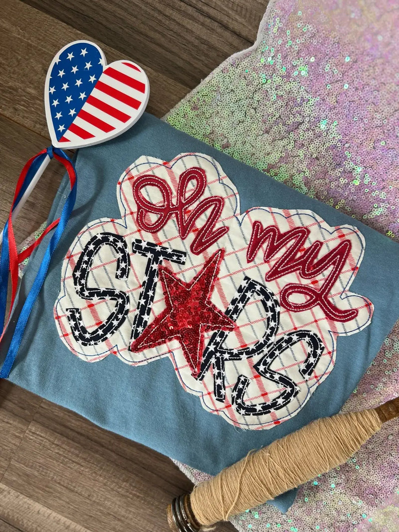 Embroidered shirt with 'Oh my stars' design and heart-shaped American flag on a glittery surface.