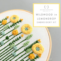 Embroidery kit with yellow flowers and green leaves on a white fabric, branded 'and other adventures embroidery co'.