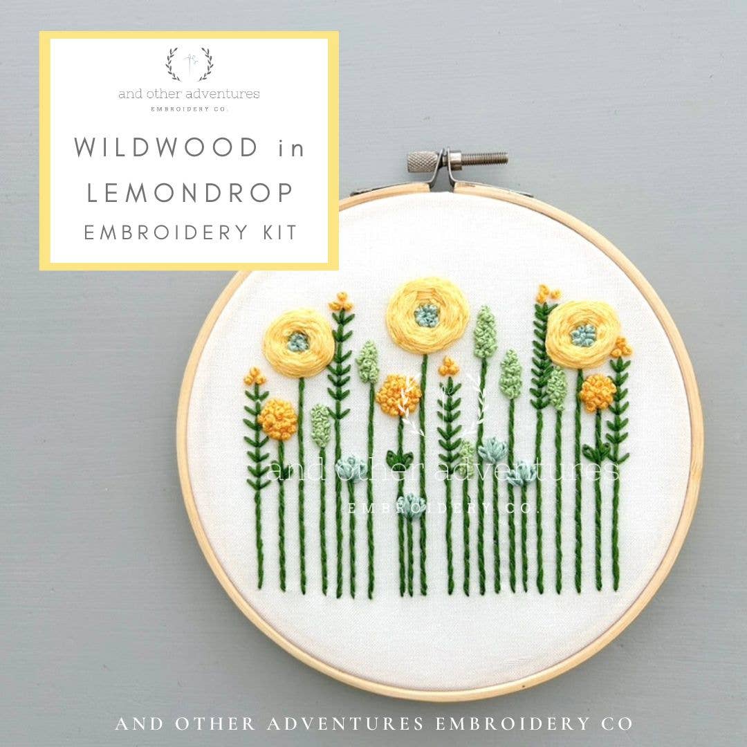 Embroidery hoop with floral design on a gray background, featuring 'Wildwood in Lemondrop' embroidery kit by And Other Adventures Embroidery Co.
