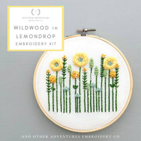 Embroidery hoop with floral design on a gray background, featuring 'Wildwood in Lemondrop' embroidery kit by And Other Adventures Embroidery Co.