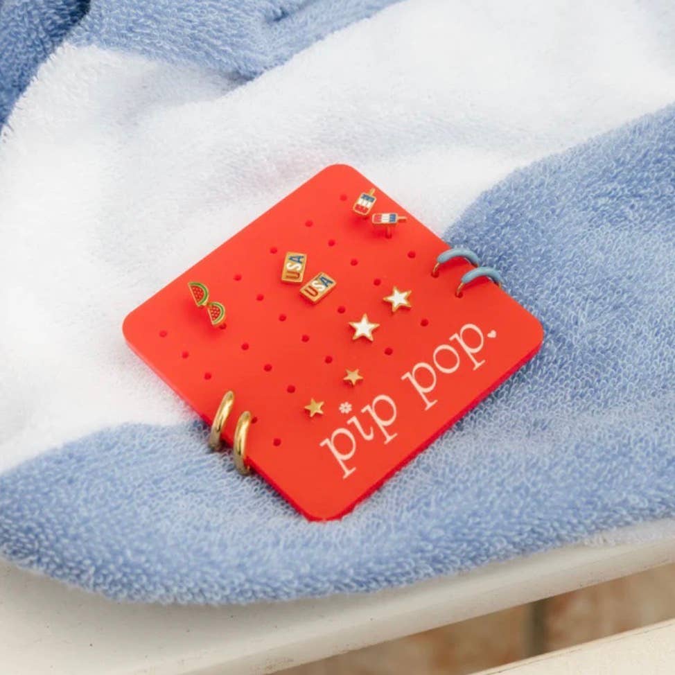 Red 'pip pop' earring holder with gold earrings on a blue and white fabric background