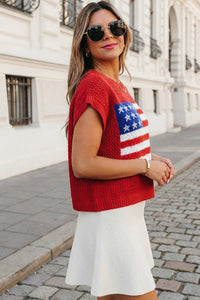 Woman wearing a red sweater with an American flag design on a street.