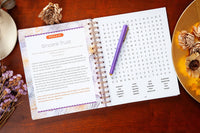 Open spiral-bound book with word search puzzle on a wooden surface with decorative elements.