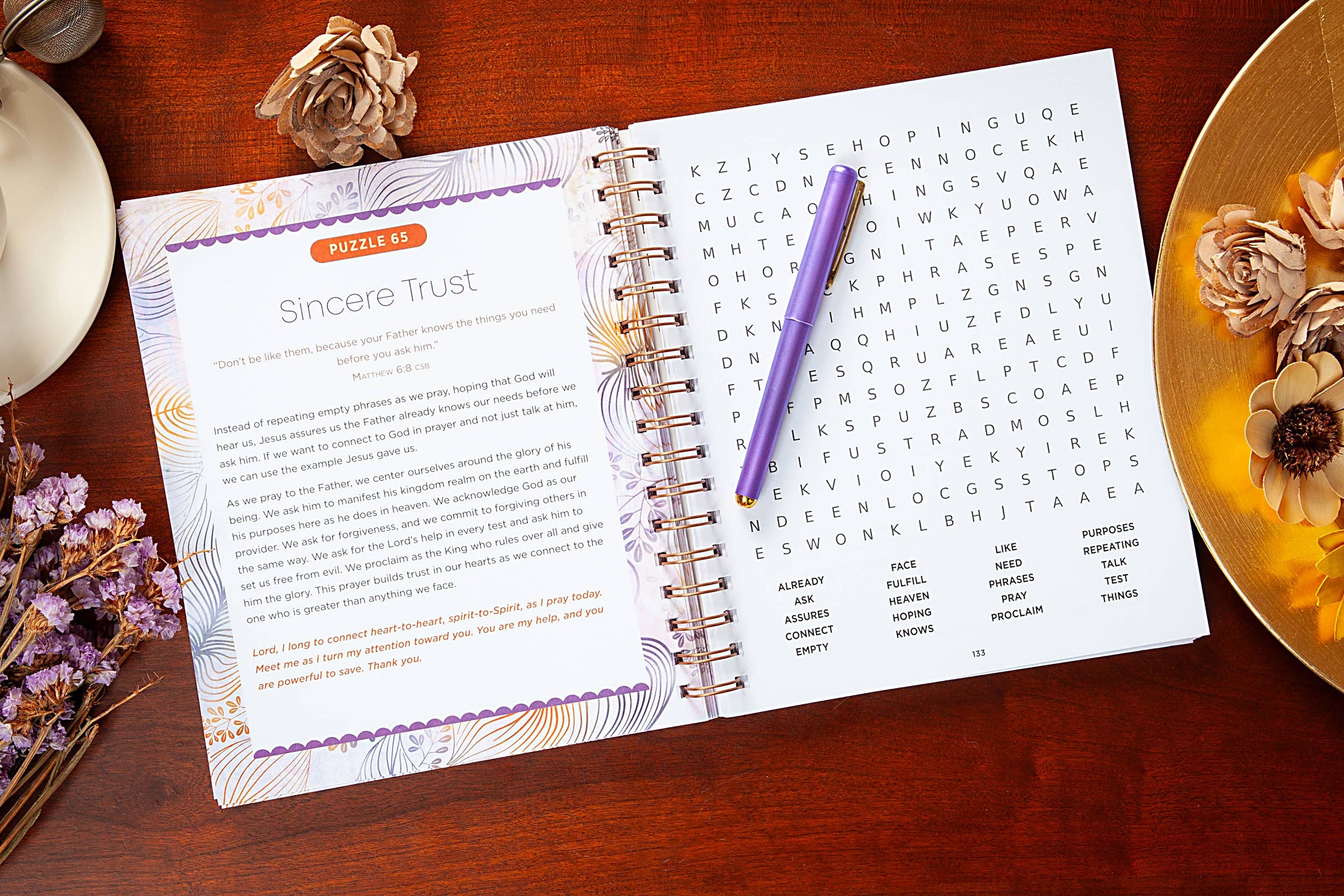Open spiral-bound book with word search puzzle on a wooden surface with decorative elements.