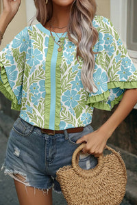 Woman wearing a floral blouse and denim shorts, holding a woven bag.