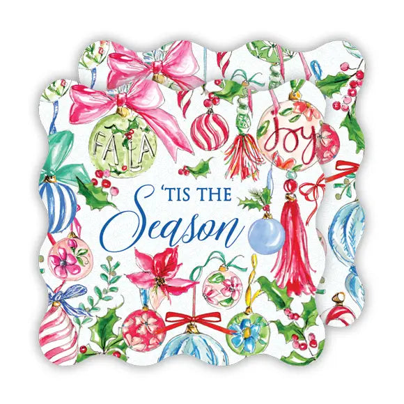A scalloped white paper napkin or decorative paper with a colorful Christmas watercolor pattern, featuring ornaments, bows, holly, and the text 'FALALAJoy Tis the Season'.