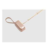 Rose gold handbag with a long strap on a light gray background