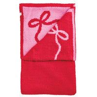 A folded red plush towel with a pink reverse side featuring a raised red bow design outlined in white, shown on a plain white background.