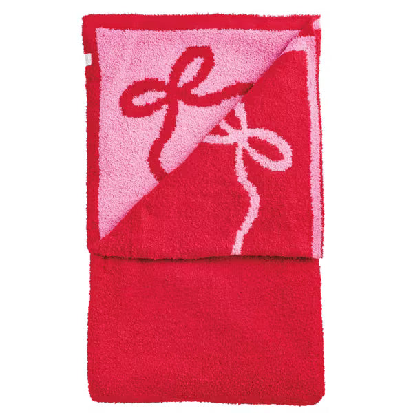 A folded red plush towel with a pink reverse side featuring a raised red bow design outlined in white, shown on a plain white background.