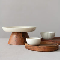 Wooden serving platter with a wooden stand and white ceramic bowls on a neutral background