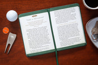 Open book on a wooden surface with golf accessories and a cup of coffee.