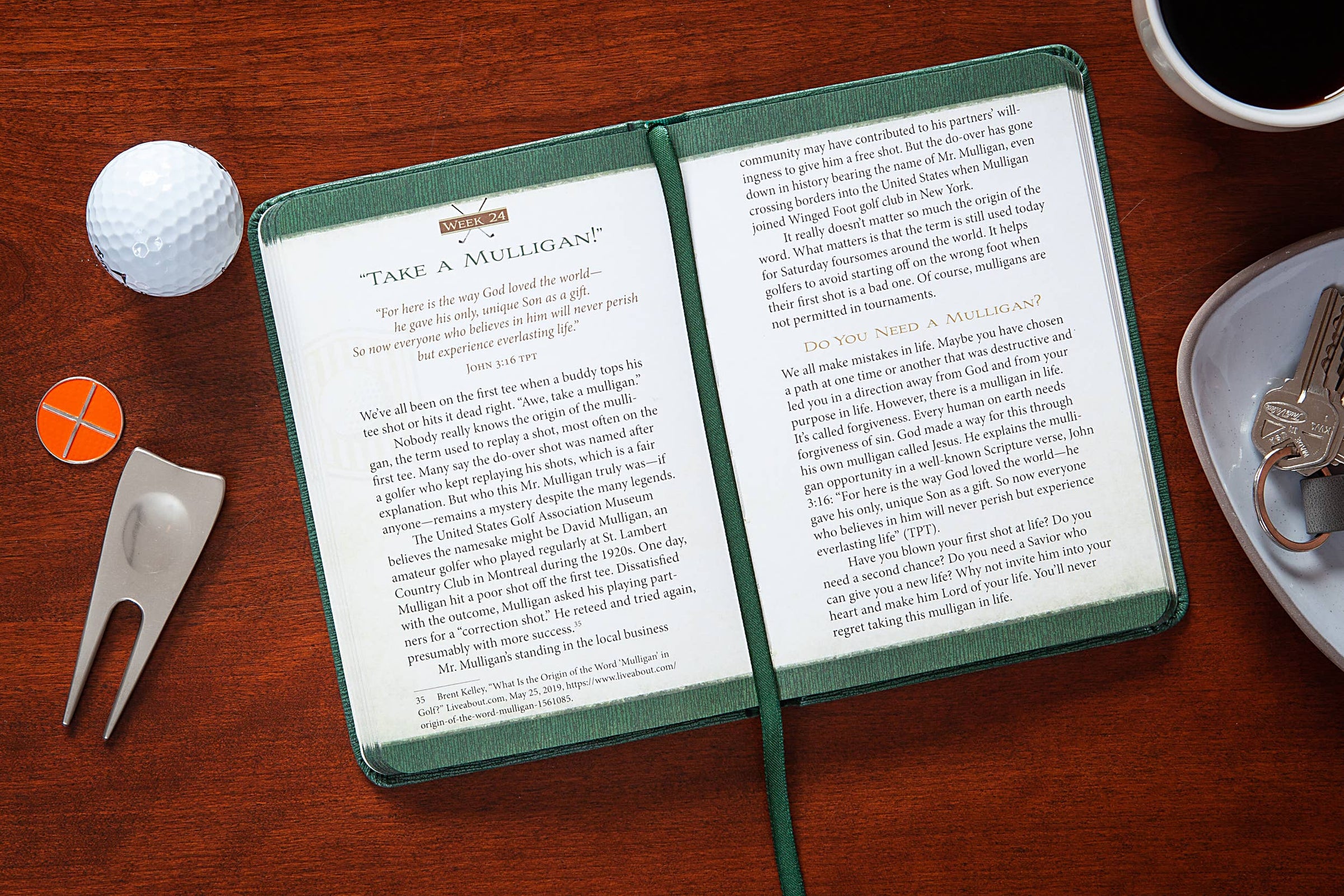 Open book on a wooden surface with golf accessories and a cup of coffee.