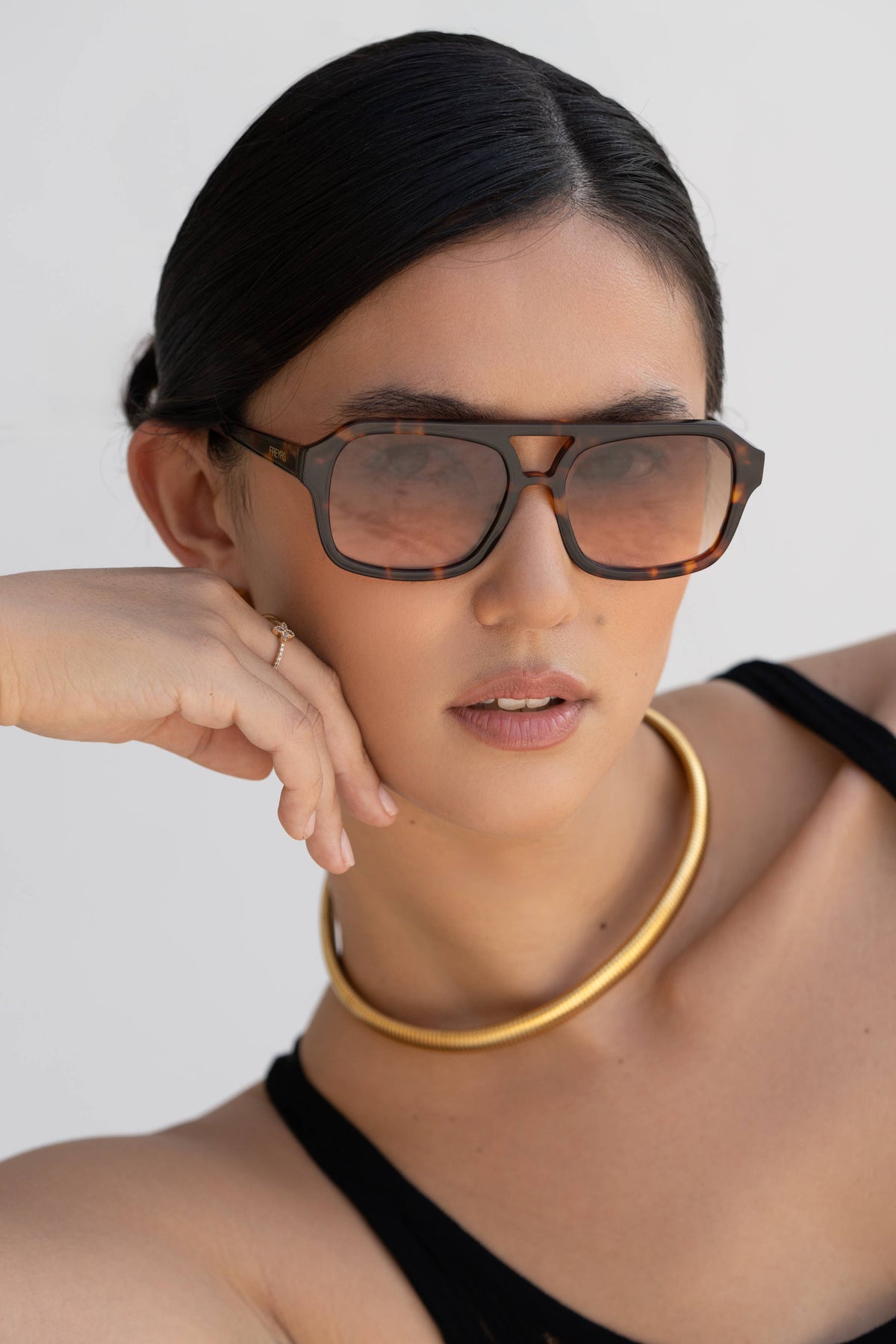 Person wearing glasses and a gold necklace against a plain background