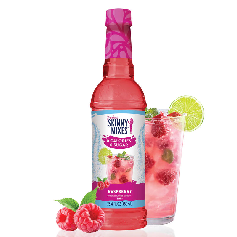 Skinny Mixes raspberry syrup bottle with a glass of raspberry juice and lime wedge on a white background