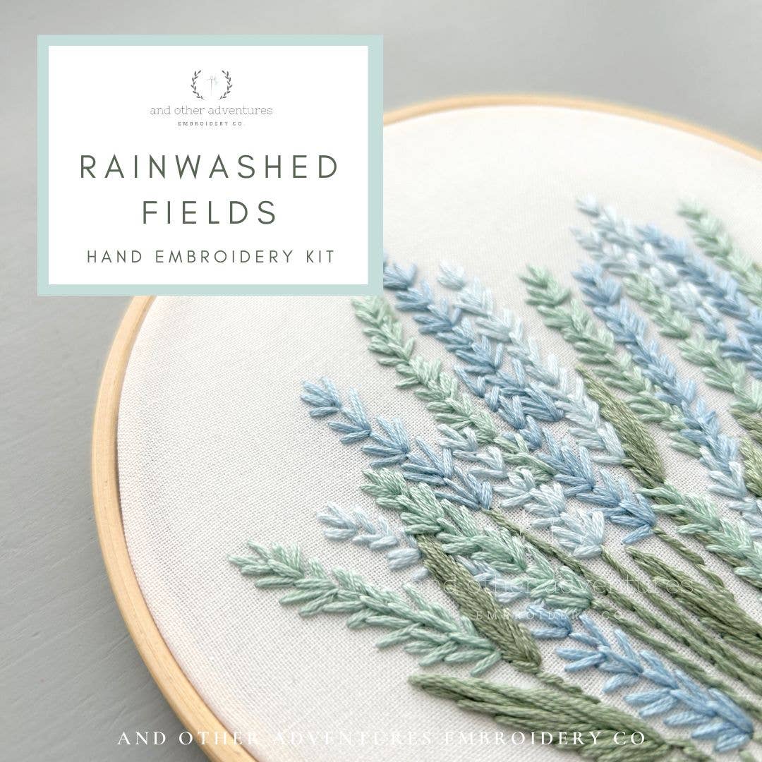 Hand embroidery kit with embroidered plants on a gray background, featuring the brand 'Rainwashed Fields'.