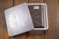 Brown leather wallet in a metal box with 'Red Wing' branding on a wooden surface